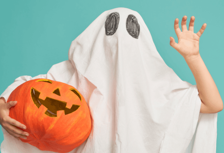 Image of a child dressed as a ghost with a pumpkin. Delwedd o blentyn wedi'i wisgo fel ysbryd ac yn dal pwmpen.