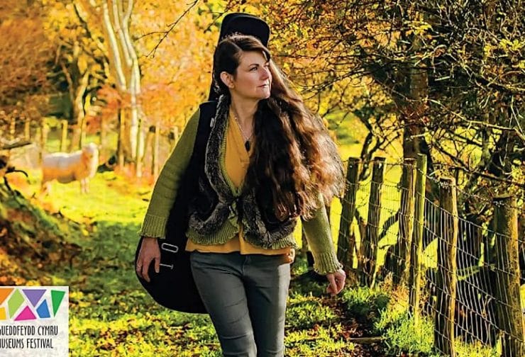 Image of Catrin O'Neill walking with her guitar on her back. Delwedd o Catrin O'Neill yn cerdded gyda'i gitar ar ei chefn.