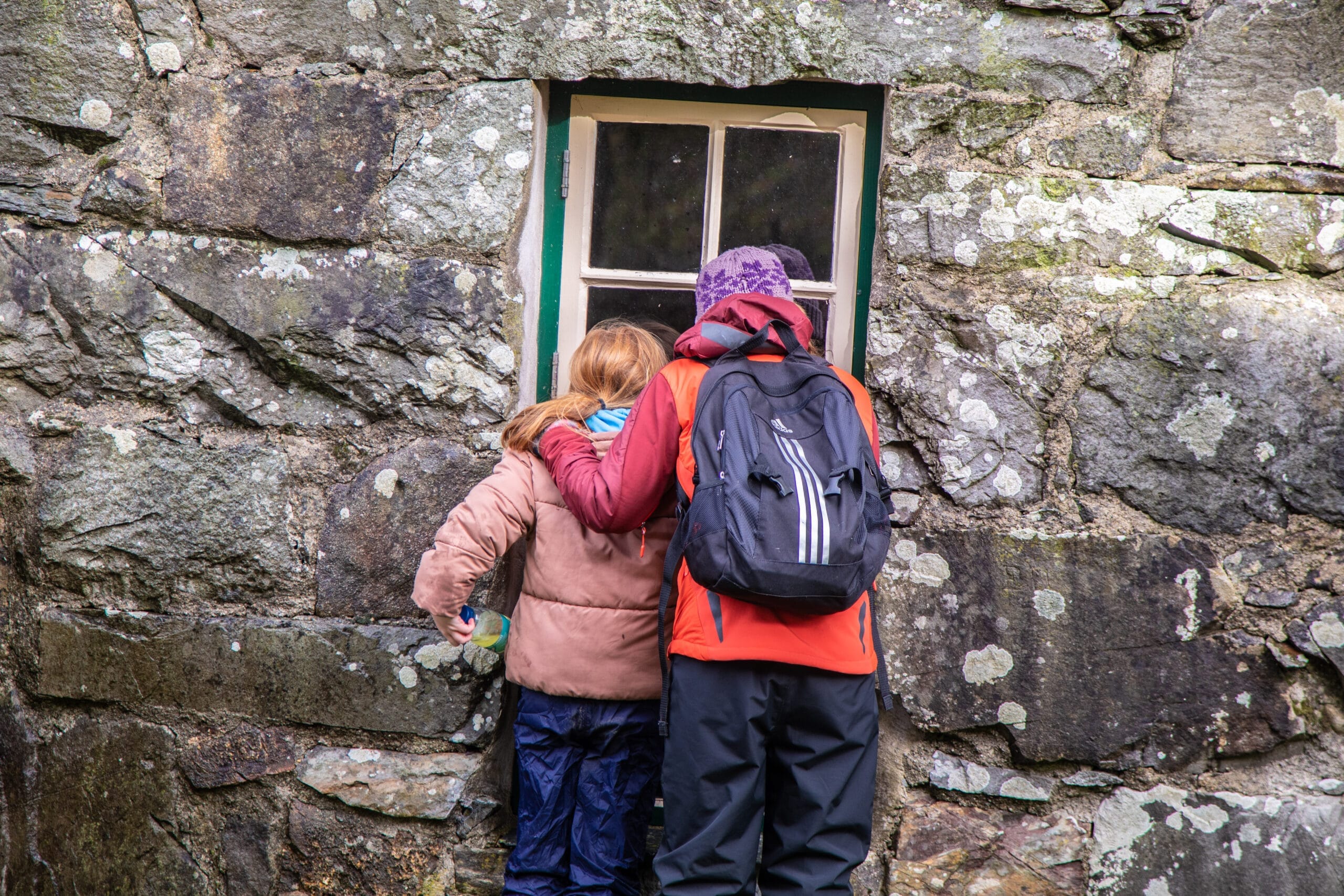 Adult and child peer into window of old building.